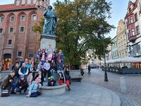 Uczniowie siedzą przed pomnikiem Mikołaja Kopernika.