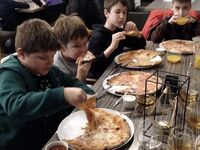 Uczniowie siedzą przy stolikach i jedzą pizzę.