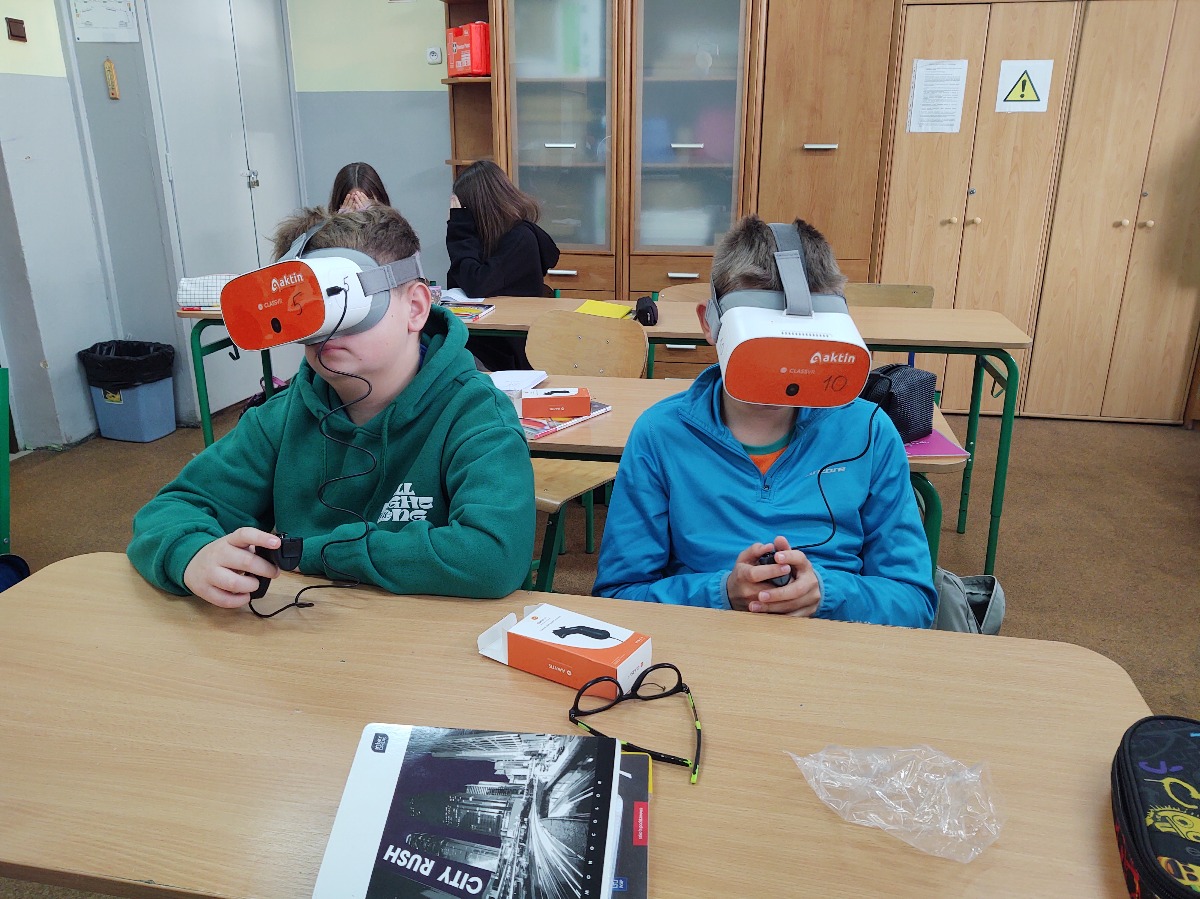 Dwóch uczniów siedzi w ławce w okularach VR
