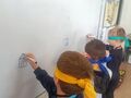 Trzech chłopców z zasłoniętymi oczami rysuje na tablicy. Wykonują zadanie.