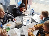 Czworo uczniów siedzi przy stoliku i jedzą hamburgery.